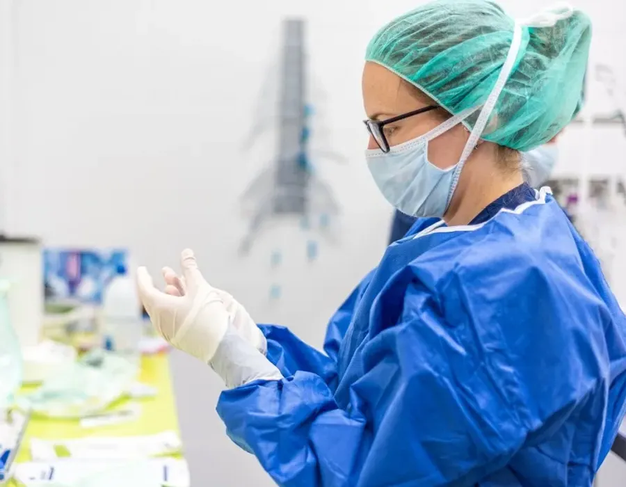 Sterile processing tech wearing mask and additional PPE cleaning surgical instrument in clean room